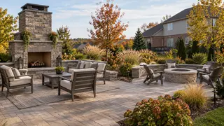 Kansas City-style backyard patio with a masonry fireplace, stone fire pit, seating, and October plantings.