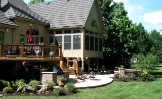 Backyard paver patio with a grill island and planting beds beneath a raised deck and screened porch